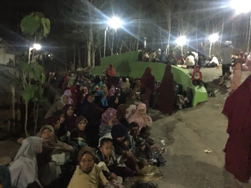 Jamaah mulai berdatangan dan duduk di pinggiran jalan di bawah lapangan.